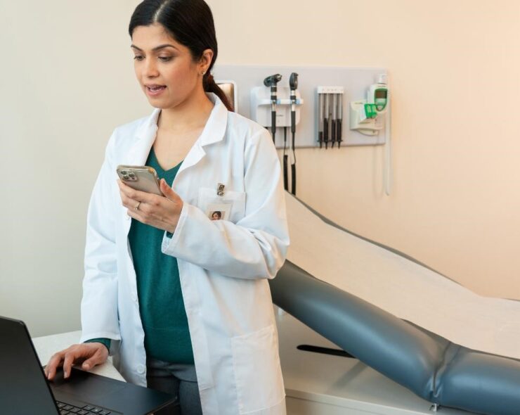 A female physician in an exam room, dictating on her mobile phone.