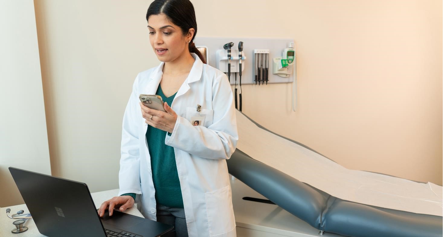 A female physician in an exam room, dictating on her mobile phone.