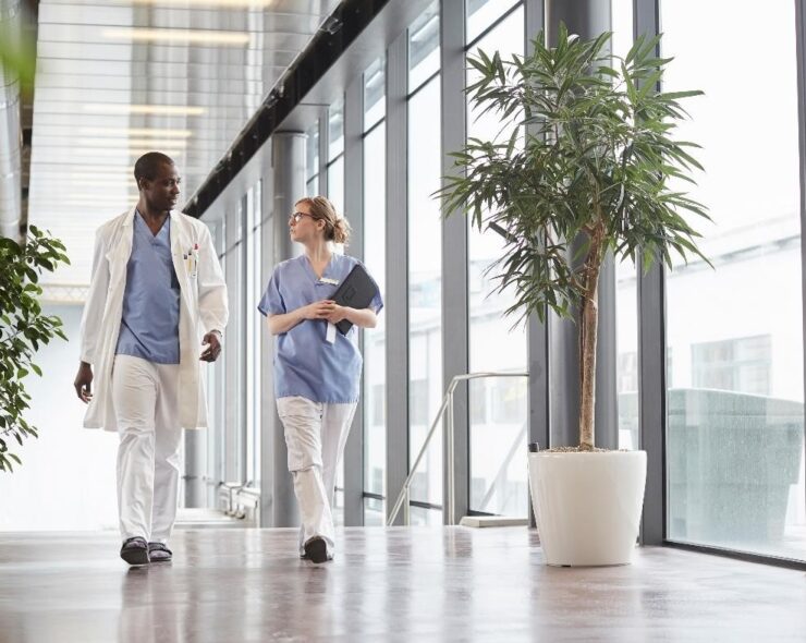 Full length of mid adult nurse discussing with doctor while walking by window in corridor at hospital