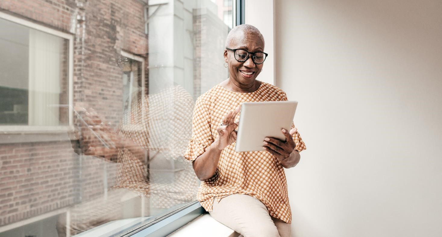 A senior woman sitting on a window-sill looking at a tablet