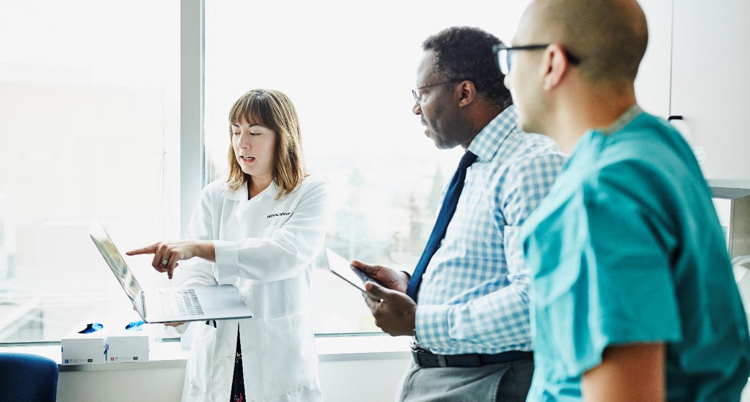 Female doctor holding laptop discussing patient information with medical team in exam room - stock photo