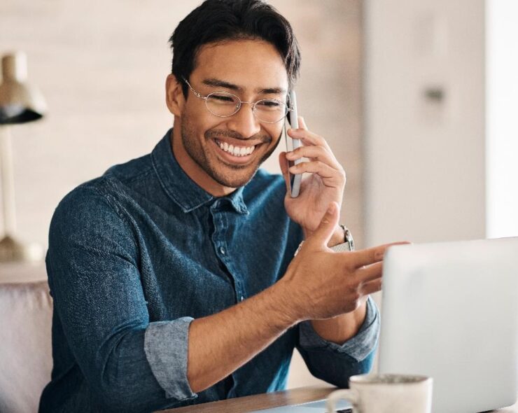 Smiling man sitting in front of his computer talking to his primary care physician on the phone.