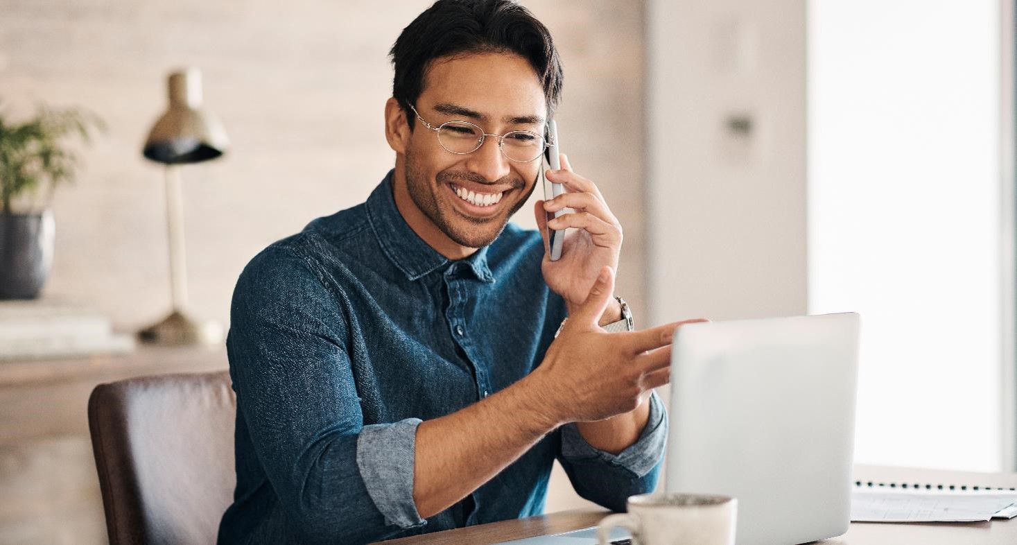 Smiling man sitting in front of his computer talking to his primary care physician on the phone.