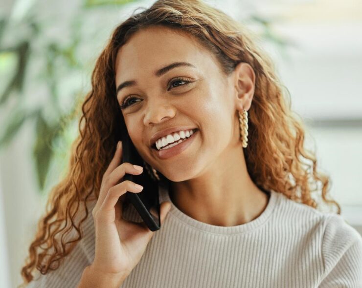 Young woman with long hair with a cell phone held up to her right ear, smiling