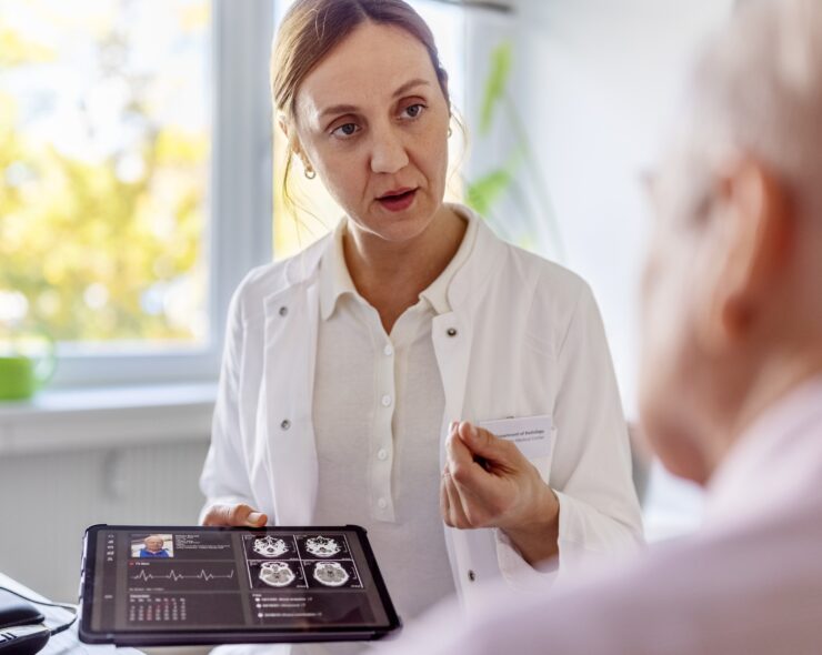 Doctor using a digital tablet to discuss a brain scan with a senior patient in clinic