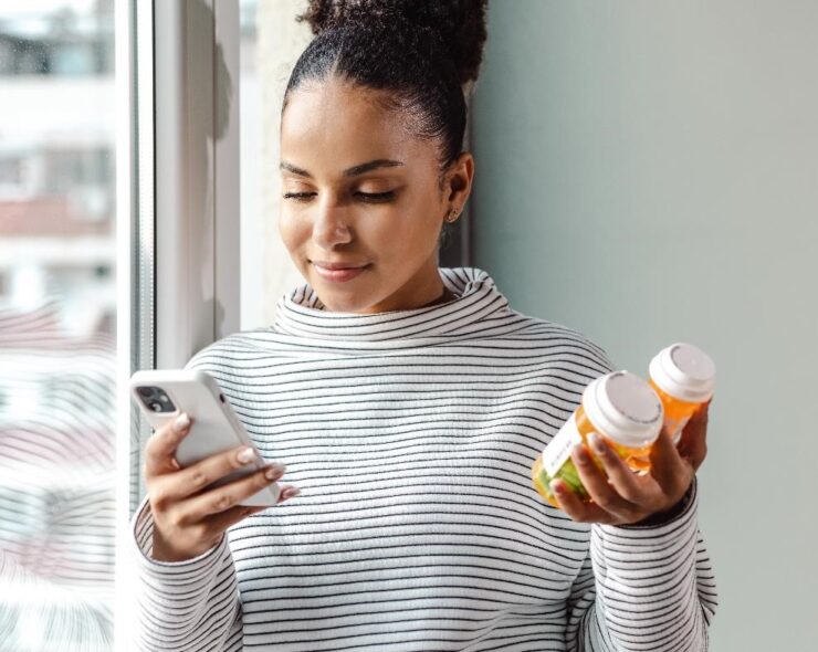 A young happy woman holding a smart phone and a pill bottle