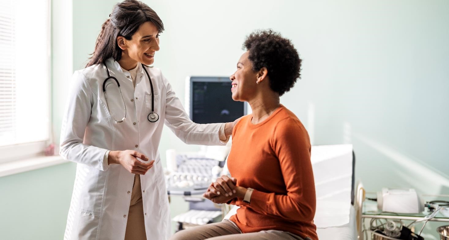 A smiling doctor talking to a patient, reassuring her with her hand on her shoulder.