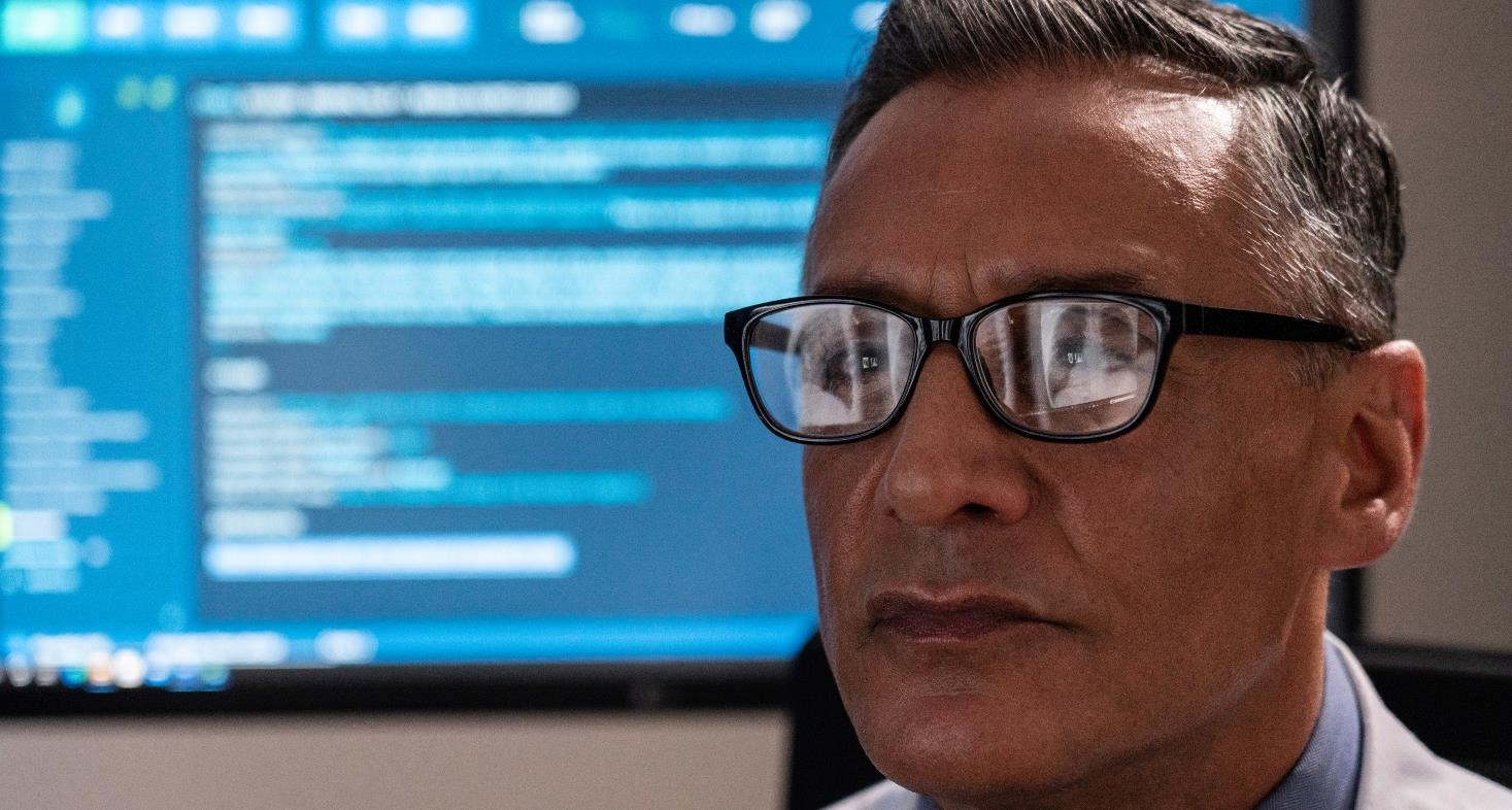 A close up of a male radiologist looking at an x-ray with the reflection showing in his spectacles.