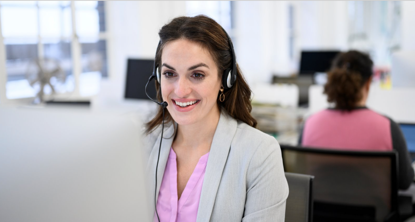 Businesswoman in her 30s seated at a desktop PC talking on a headset