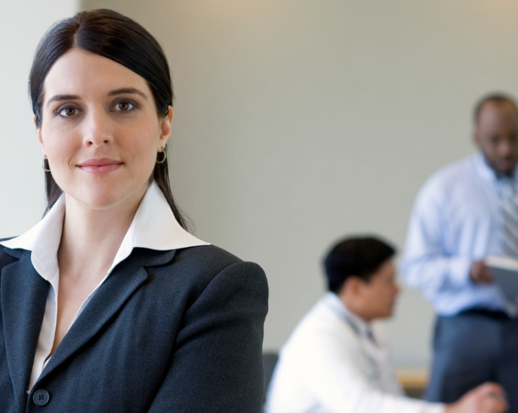 A young business woman standing in front of her colleagues against a grey background